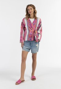 Krāsains audums josta ar rozā rakstiem uz gaiša fona, apvienota ar izsistiem džinsu šortiem un rozā strukturētām slaidām.