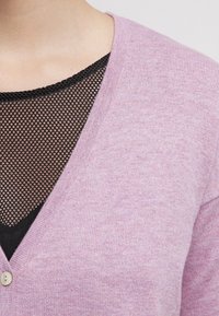Light purple cardigan with a V-neck design, featuring soft texture and a single button, layered over a black mesh top.