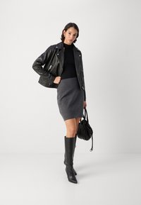 Zwarte leren motorjack, aansluitend zwart top, grijze breigoed mini-jurk, hoge zwarte laarzen tot de knie en een kleine zwarte handtas. Gladde texturen, gelaagd ontwerp.
