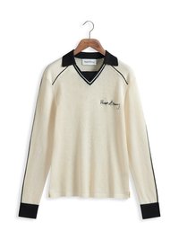 Chemise à manches longues en maille de couleur crème, avec un col et des poignets noirs, présentant un décolleté en V et des lignes d'accent noir. Logo brodé sur le devant.
