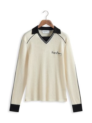 Chemise à manches longues en maille de couleur crème, avec un col et des poignets noirs, présentant un décolleté en V et des lignes d'accent noir. Logo brodé sur le devant.