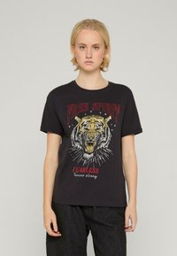 Melnas kokvilnas T-krekls ar tīģera grafiku un uzrakstiem "BRĪVS GARS" un "NEBAIDĪGS". Īsas piedurknes un apaļa kakla izgriezums.