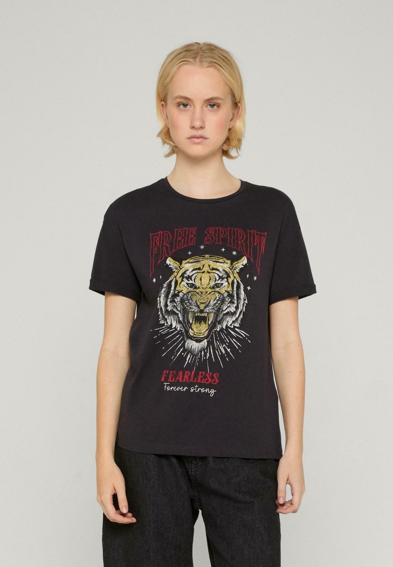 Melnas kokvilnas T-krekls ar tīģera grafiku un uzrakstiem "BRĪVS GARS" un "NEBAIDĪGS". Īsas piedurknes un apaļa kakla izgriezums.