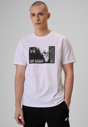 Młody mężczyzna z ogoloną głową w białej koszulce z czarną grafiką snowboardzisty oraz napisami "RIDE" i "OFF SCRIPT."