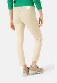 Jeans ajustados beige con una textura suave, bolsillos traseros y una cinturilla baja, combinados con zapatos gruesos beige. Suéter verde visible por encima.