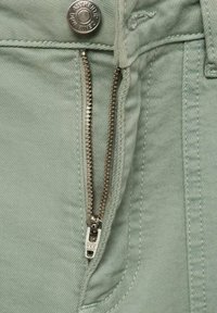 Ljusgrön denimtyg med en silverfärgad dragkedja och knappstängning. Dragkedjan har en märkesdragtab och en slät yta.