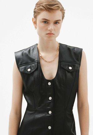 Vestido de cuero negro con un profundo escote en V, diseño sin mangas, botones a presión en la parte delantera y dos bolsillos en el pecho. Acento de cadena dorada.
