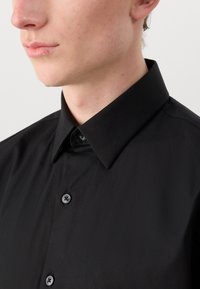 Zwarte blouse met knopen van gladde stof, klassieke kraag en grijze knopen. Heeft een getailleerd ontwerp en schone, minimalistische lijnen.