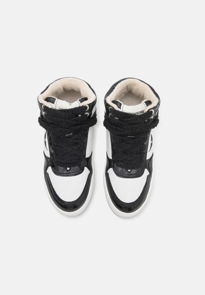 High-top sneakers featuring a black and white color scheme, textured black straps, smooth leather, and soft beige lining.