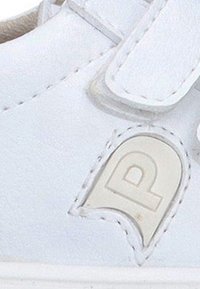 Primer plano de la sección de una zapatilla blanca con costuras cosidas y un parche de goma gris claro con forma de arco que lleva la letra "P".