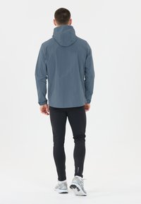 Vattentålig, ljusgrå jacka med huva, elastiska ärmslut och normal passform. Bärs över svarta träningsleggings och löparskor.