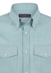 Camisa de botones de color azul claro hecha de tela texturizada. Presenta un cuello puntiagudo, dos bolsillos en el pecho y botones blancos. Etiqueta de la marca visible.