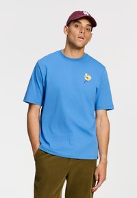 Camiseta de algodón azul de manga corta con cuello redondo, con un bordado de flor amarilla en el pecho y un corte holgado.