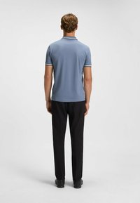 Blaues Polohemd mit Slim Fit, kurzen Ärmeln und weißen Akzenten; kombiniert mit schwarzen Hosen und schwarzen Schuhen, von hinten gesehen.