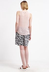Haut sans manches rose clair avec une ouverture en forme de clé dans le dos, associé à une jupe à imprimé floral noir et blanc en tissu doux. Sandales blanches à enfiler.