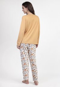 Top amarillo de manga larga combinado con pantalones de pijama blancos que presentan divertidos patrones de animales en gris y naranja. Tela suave y ligera.