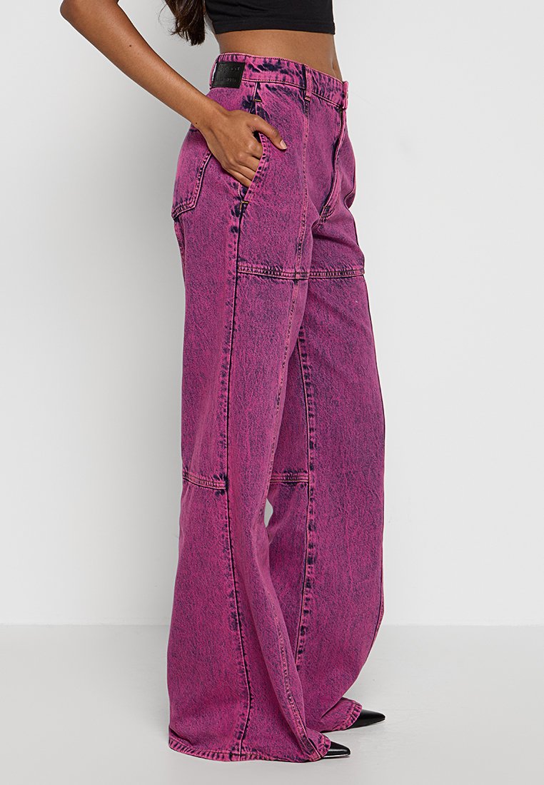 Jeans a vita alta e gamba larga in denim rosa brillante con una texture sbiadita, dotati di tasche frontali e cuciture dettagliate lungo le cuciture.
