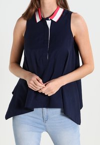 Top senza maniche blu navy con colletto bianco e dettagli rossi, patta con bottoni e vestibilità ampia, realizzato in morbido tessuto intrecciato.