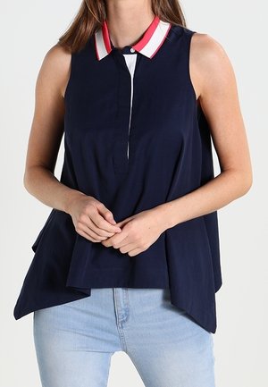 Top sin mangas en color navy con un cuello blanco y detalles rojos, tapeta de botones y un corte holgado, confeccionado en una suave tela tejida.