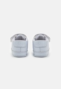 Ljusblå barnskor i sneakersstil med en slät läderutsida, kardborreband och präglad "BOSS"-logotyp på hälen. Rundad tådesign.