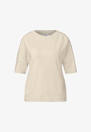 Beżowa koszulka z krótkim rękawem, wykonana z miękkiej bawełny, z okrągłym dekoltem, luźnym krojem i guzikami na ramionach.