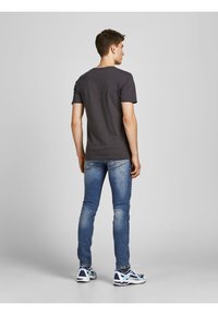 Siva bombažna majica, kratki rokavi, okrogla izrezana, v kombinaciji z modrimi jeans hlačami in večbarvnimi športnimi čevlji z belim podplatom.