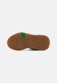 Suela de zapato gris con un diseño texturizado y acanalado. Presenta una base de goma marrón y un logo verde. La suela es plana y está diseñada para ofrecer tracción.