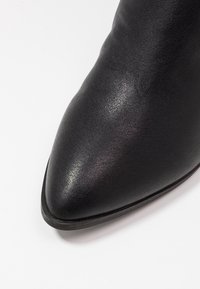 Zwarte leren enkelboot met een spitse neus en een gestructureerd oppervlak, met een minimalistisch ontwerp en een platte zool.