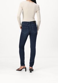 Jeans ajustados de color azul oscuro con cinco bolsillos, diseño limpio y detalles de costura sutiles, combinados con una camiseta de manga larga de canalé claro.