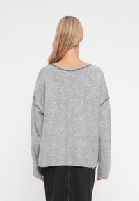 Maglione grigio a maglia con spalle scese, texture a costine e cuciture a contrasto lungo il collo e le maniche. Vista posteriore mostrata.