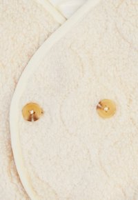 Cremfarbener Fleece-Weste mit strukturiertem Finish, mit einem V-Ausschnitt und zwei runden, braunen Knöpfen an der Vorderseite zum Schließen.