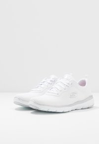 Ett par vita Skechers sportskor med mesh-övre, snörningsdesign och lätt vadderade sulor på en vit yta.