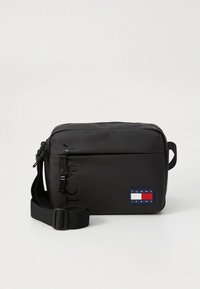 Black rectangular crossbody bag with adjustable strap, front zipper pocket, and Tommy Jeans logo patch in bottom right corner.