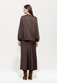 Braune Satinbluse mit langen Ärmeln und lässiger Passform, kombiniert mit einem passenden Satinskirt. Das Outfit zeichnet sich durch ein sauberes, minimalistisches Design aus.