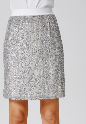 Jupe en sequins argentés avec une ceinture élastique blanche. Le tissu a une finition texturée et scintillante, et la jupe arrive au-dessus des genoux.