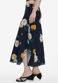 Blomstrende maxi-nederdel med sort baggrund og gule samt hvide tusindfryd, lavet af letvægtsstof, med en sideslids og flydende design.