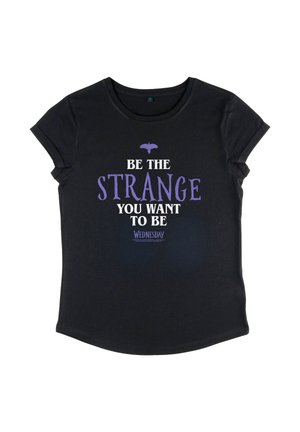 T-shirt noir à manches courtes avec un graphisme de chauve-souris violette et le texte "Soyez l'étrange que vous voulez être" en lettres blanches et violettes sur le devant.