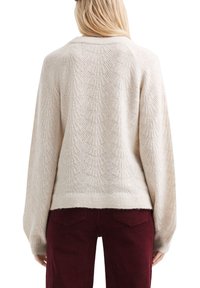 Crème gebreide trui met bladpatroon, ontspannen pasvorm en geribbelde zoom. Gecombineerd met bordeaux corduroy broek. Zachte textuur en lichtgewicht materiaal.