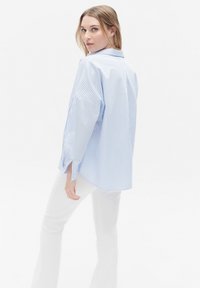 Blauw-wit gestreept shirt met een ontspannen fit, drop schouders en zijsplitten, gecombineerd met witte aansluitende broek.