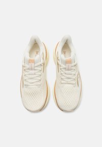 Baskets de course légères en crème avec une tige en mesh, des lacets ton sur ton et des accents subtils en orange sur le talon et le logo. Semelle douce et rembourrée.
