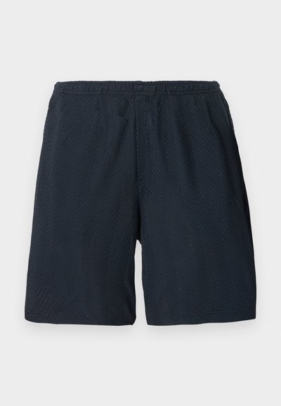 Shorts noirs mi-longue avec taille élastique et motif texturé en chevrons subtils, présentés sur un fond clair uni.