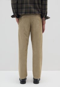 Pantaloni in corduroy beige con vestibilità dritta, dotati di tasche posteriori e superficie testurizzata. Indossati con una camicia a quadri scuri e scarpe nere.
