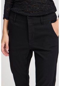 Black, tapered trousers with side pockets, made of a smooth cotton blend. Features a zip fly and belt loops, minimal stitching detail.