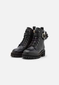Botas negras de cuero hasta el tobillo con suela gruesa, que presentan herrajes dorados, cordones en la parte delantera, detalles con hebilla y un acento decorativo de flor.