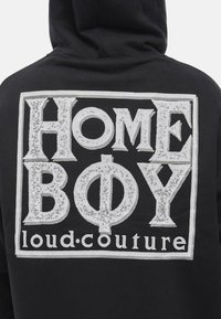 Felpa nera con cappuccio caratterizzata da una grande stampa grafica bianca con le parole "HOME BOY" e "loud.couture" in un carattere audace e invecchiato.