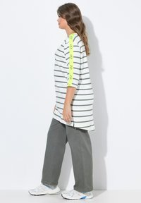 Gestreepte lange tuniek in wit en groen, met een neongele accent op de mouwen. Combinatie met grijze wijde broek en witte sneakers.