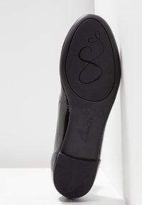 Semelle d'une chaussure de ville noire avec une surface antidérapante texturée, un motif décoratif en spirale près de l'orteil, et le nom de la marque Clarks embossé sur la voûte plantaire.