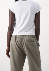 Bílý krátký rukáv tričko v kombinaci s volnými olivově zelenými kalhotami s kapsou na zadní části a třepeným lemem. Měkký textil s pohodlným střihem.
