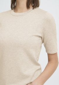 T-shirt en tricot beige avec encolure ronde, manches courtes et texture lisse. Présente un design simple et des coutures discrètes près des épaules.