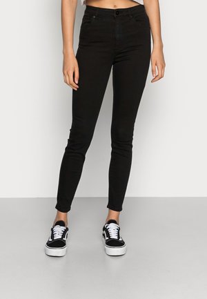 Jeans ajustados negros de mezclilla, con una cintura alta, diseño estándar de cinco bolsillos y cierre de botón, combinados con zapatillas negras.